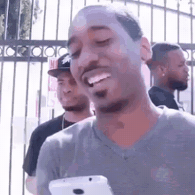 A Man Is Holding A Cell Phone And Smiling While Standing In Front Of A Fence . GIF