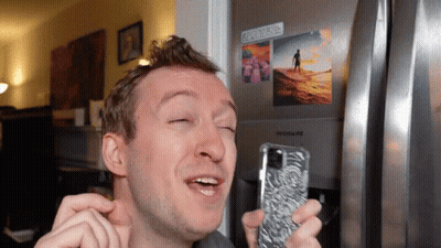 A Man Is Holding A Cell Phone In Front Of A Frigidaire Refrigerator GIF