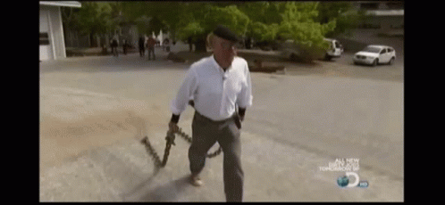 A Man Is Holding A Chain Around His Waist While Walking Down A Street . GIF