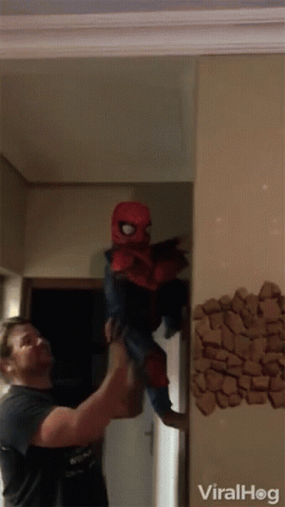 A Man Is Holding A Child In A Spiderman Costume In Front Of A Wall That Says Viralhog GIF