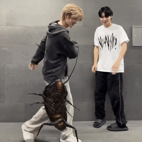 A Man Is Holding A Cockroach While Another Man Stands Next To Him . GIF