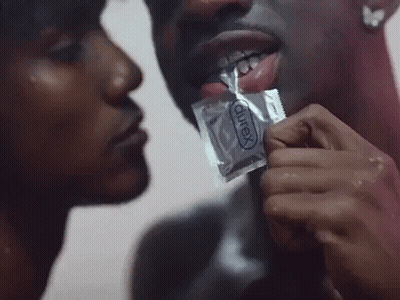 A Man Is Holding A Condom In His Mouth While A Woman Kisses Him GIF
