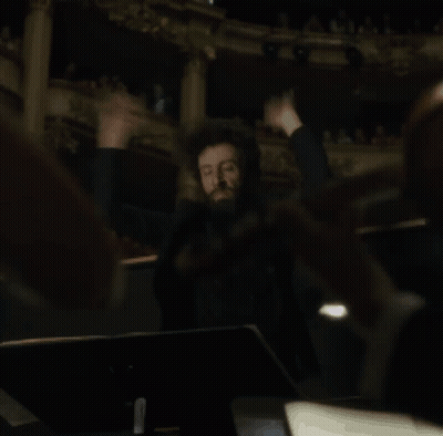 A Man Is Holding A Conductor 'S Baton In His Hands In A Dark Room GIF