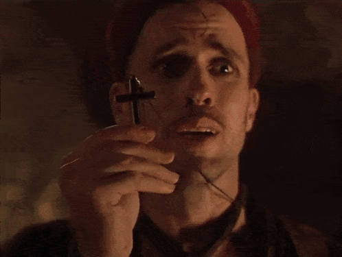 A Man Is Holding A Cross In His Hand And Making A Face GIF