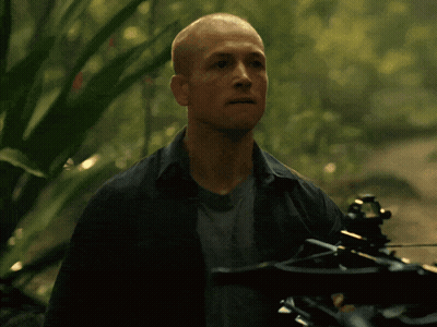 A Man Is Holding A Crossbow In The Woods And His Mouth Is Open GIF