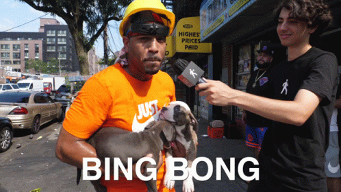 A Man Is Holding A Dog In Front Of A Sign That Says Higher Prices Paid GIF