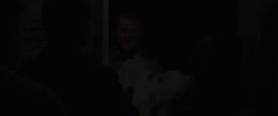 A Man Is Holding A Dog In His Arms While Standing In Front Of A Group Of People In A Doorway . GIF