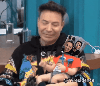 A Man Is Holding A Doll With A Picture Of A Man And A Woman Behind Him GIF