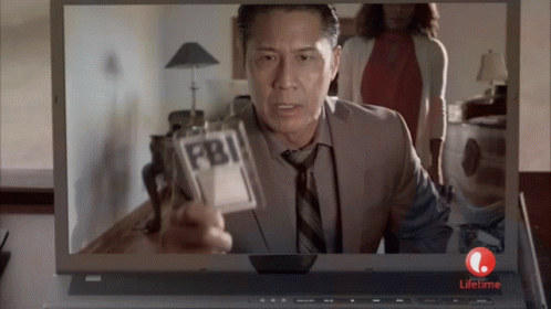 A Man Is Holding A Fbi Badge In Front Of A Laptop GIF