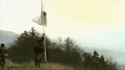 A Man Is Holding A Flag On Top Of A Pole In A Field . GIF