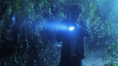 A Man Is Holding A Flashlight In His Hand In A Dark Forest . GIF