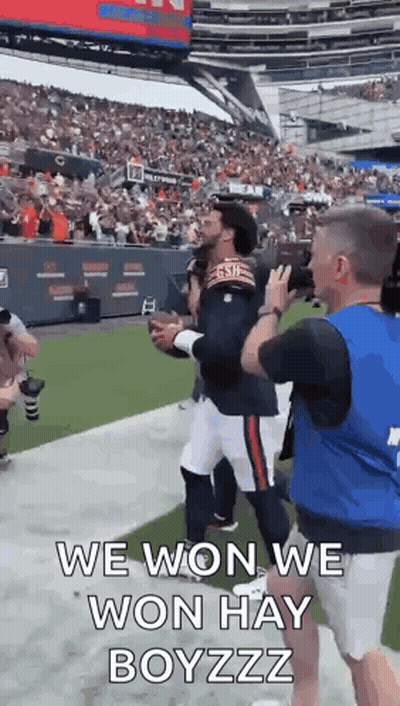 A Man Is Holding A Football In A Stadium And A Man Is Taking A Picture Of Him . GIF