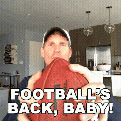 A Man Is Holding A Football With The Words " Football 'S Back Baby " Written On It GIF