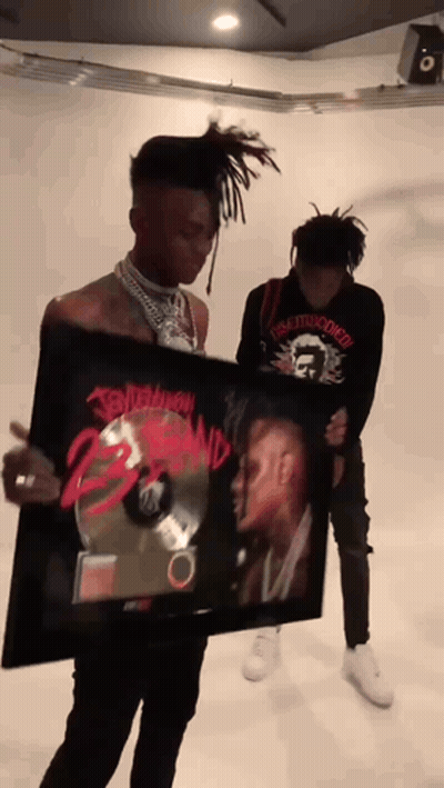 A Man Is Holding A Framed Picture Of A Man With Dreadlocks And The Word Tomorrow On It GIF
