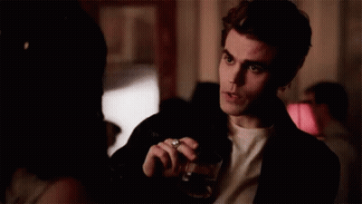 A Man Is Holding A Glass Of Wine And Smoking A Cigarette While Talking To A Woman . GIF