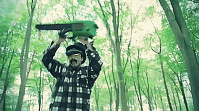 A Man Is Holding A Green Chainsaw Over His Head In The Woods . GIF