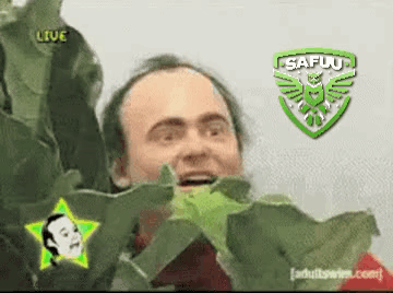 A Man Is Holding A Green Leaf In Front Of A Safuu Emblem GIF