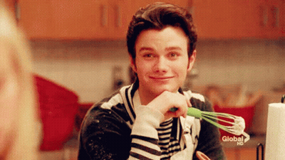 A Man Is Holding A Green Whisk In His Hand And Smiling In A Kitchen . GIF