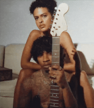 A Man Is Holding A Guitar With A Woman Sitting On His Back GIF