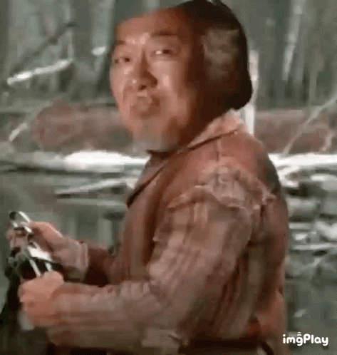 A Man Is Holding A Gun And Making A Funny Face While Standing In The Woods . GIF