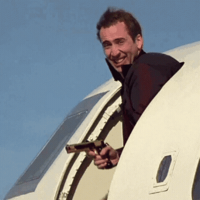 A Man Is Holding A Gun And Peeking Out Of An Airplane Window . GIF