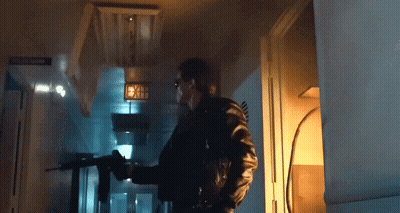 A Man Is Holding A Gun In A Dark Room With A Sign That Says Exit GIF