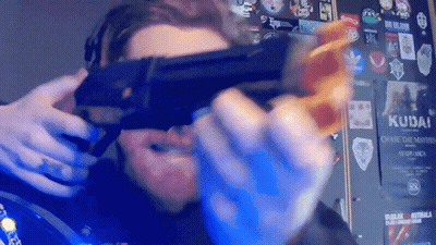 A Man Is Holding A Gun In Front Of A Wall With Stickers On It Including One That Says Kudai GIF
