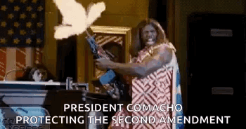 A Man Is Holding A Gun In Front Of An American Flag While A Dove Is Flying In The Air . GIF