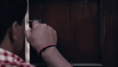 A Man Is Holding A Gun In His Hand And Looking Through A Window . GIF
