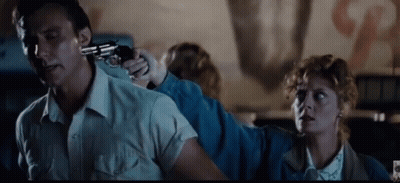 A Man Is Holding A Gun To His Head While A Woman Holds A Gun To His Back . GIF