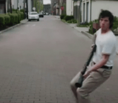 A Man Is Holding A Gun While Walking Down A Brick Street . GIF