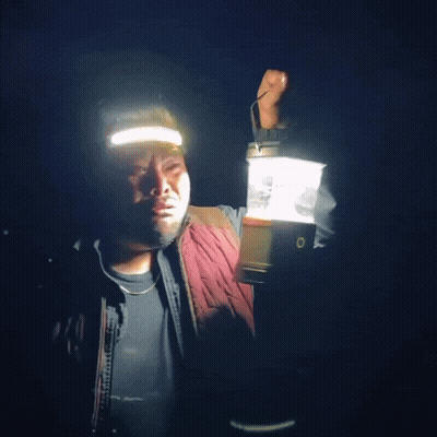 A Man Is Holding A Lantern In His Hand And Wearing A Headlamp GIF