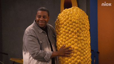 A Man Is Holding A Large Corn On The Cob In Front Of A Nick Sign GIF