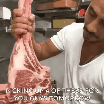 A Man Is Holding A Large Piece Of Meat In His Hands In A Kitchen . GIF