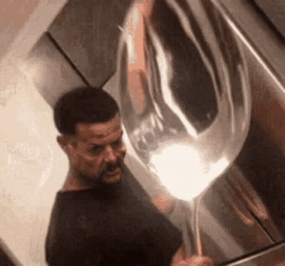 A Man Is Holding A Large Silver Balloon In His Hand . GIF