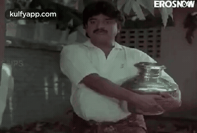 A Man Is Holding A Large Vase In His Hands . GIF