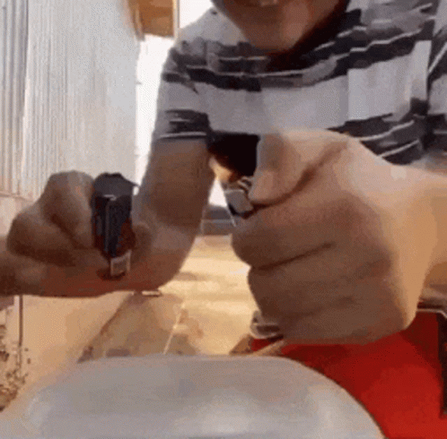 A Man Is Holding A Lighter In His Hand While Sitting At A Table . GIF