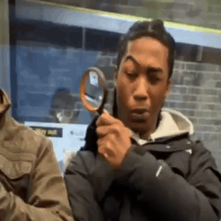 A Man Is Holding A Magnifying Glass And Looking Through It . GIF
