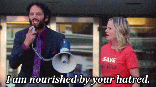 A Man Is Holding A Megaphone Next To A Woman Who Is Wearing A Red Shirt That Says Save Us Rock GIF