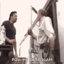 A Man Is Holding A Microphone And Talking To Another Man While Standing In Front Of A Truck . GIF