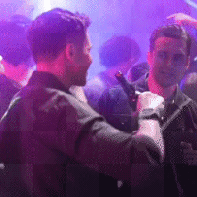 A Man Is Holding A Microphone In A Crowded Room GIF