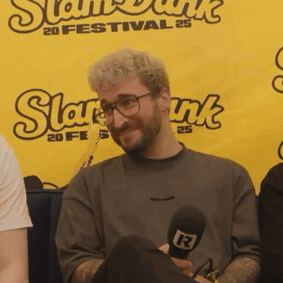A Man Is Holding A Microphone In Front Of A Banner That Says Slam Dunk GIF