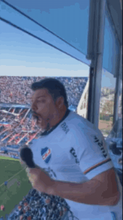 A Man Is Holding A Microphone In Front Of A Crowd At A Soccer Game .. GIF