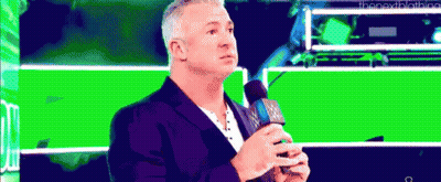A Man Is Holding A Microphone In Front Of A Green Background . GIF