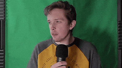 A Man Is Holding A Microphone In Front Of A Green Screen And Making A Funny Face . GIF