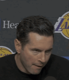 A Man Is Holding A Microphone In Front Of A Lakers Logo GIF