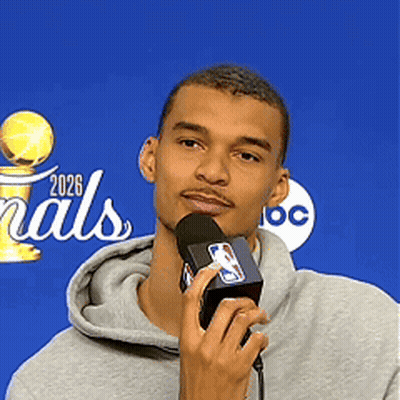 A Man Is Holding A Microphone In Front Of A Sign That Says Finals 2026 GIF