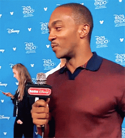 A Man Is Holding A Microphone In Front Of A Wall That Says Disney Expo GIF