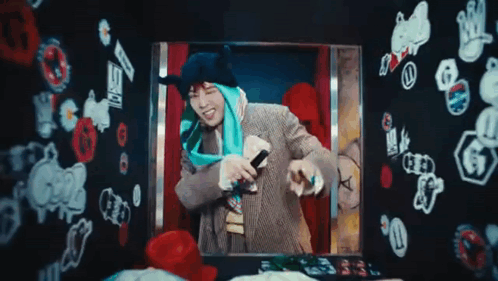 A Man Is Holding A Microphone In Front Of A Wall With Stickers On It GIF