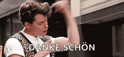 A Man Is Holding A Microphone In His Hand And Saying `` Danke Schön '' In German . GIF